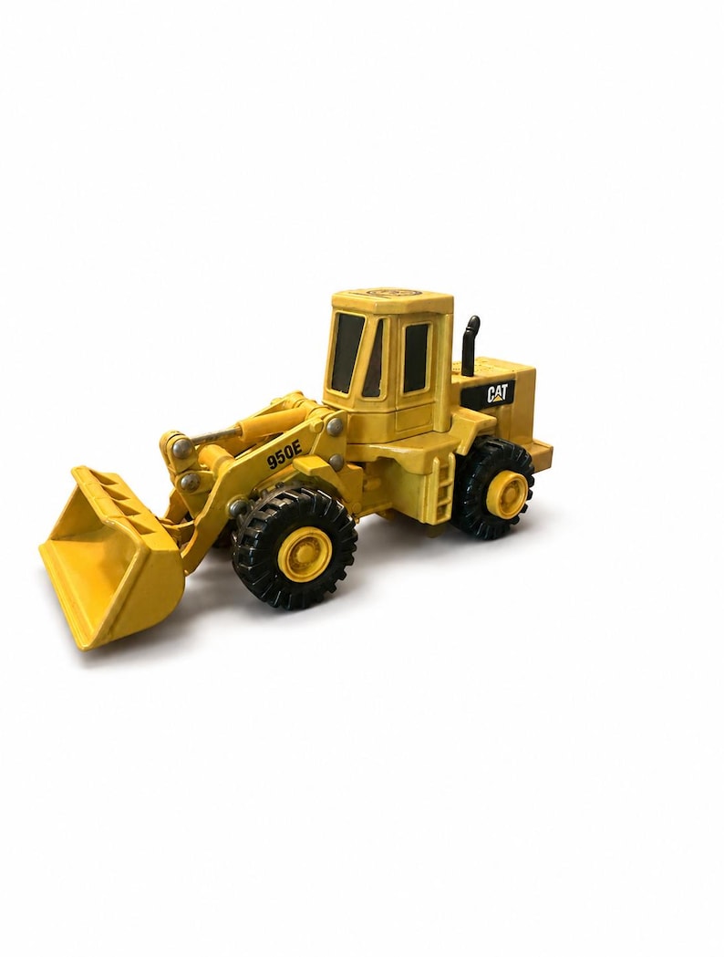 May include: A yellow CAT 950E wheel loader toy vehicle featuring a front bucket, black tyres with yellow hubs, and a cabin with black windows. The construction equipment model displays the CAT logo on the side and the model number 950E on the arm.