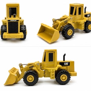May include: A yellow Caterpillar 950E wheel loader toy vehicle featuring a front bucket, black tyres, and a cabin with black windows. The model displays the Caterpillar brand name on the front grille and the CAT logo on the rear side panel.