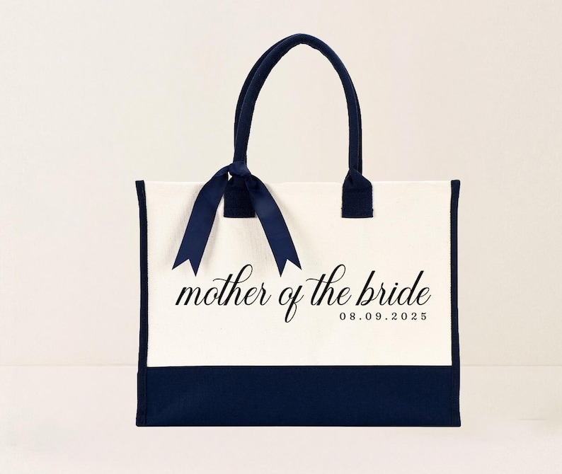 Canvas tote bag featuring the text “Mother of the Bride” in elegant script with a custom date printed underneath; designed on a two-tone cotton canvas tote with sturdy handles and a ribbon accent; displayed in a neutral soft-lit background; perfect personalized wedding gift for mothers, brides, or bridal parties.