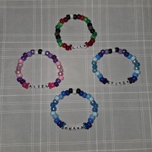 May include: Four colourful beaded bracelets. One bracelet has red, green, black, and white beads with the name "LILO". Another has pink, purple, and white beads with "ANGEL". A third has blue beads with "STITCH". The last has blue beads with "OHANA".