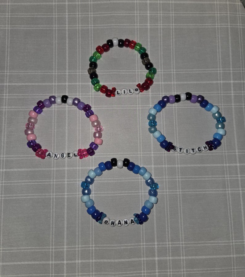 May include: Four colourful beaded bracelets. One bracelet has red, green, black, and white beads with the name "LILO". Another has pink, purple, and white beads with "ANGEL". A third has blue beads with "STITCH". The last has blue beads with "OHANA".
