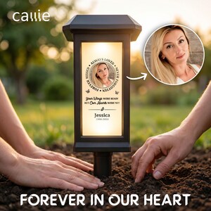 May include: A black solar-powered memorial garden light with a rectangular illuminated panel. The panel features a circular photo of a person, the text "ALWAYS LOVED NEVER FORGOTTEN", "YOUR WINGS WERE READY BUT OUR HEARTS WERE NOT", "Jessica", and "1990-2026".