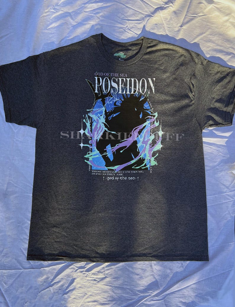 May include: Dark gray t-shirt featuring a graphic of Poseidon, the Greek god of the sea, with the text "POSEIDON" and "GOD OF THE SEA." The design includes blue, purple, and green accents. The shirt also has the text "THESE MORTALS DO CONCERN ME, DIVING AS THEY ARE" and "god of the sea."