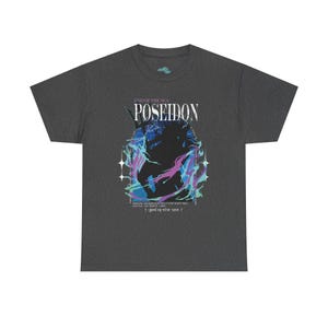 May include: Dark gray t-shirt featuring the word "POSEIDON" above a graphic of the sea god. The design includes blue and purple accents, with text that reads "GOD OF THE SEA" and a quote at the bottom. A casual tee.