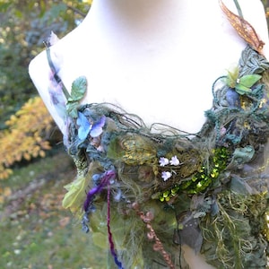 Peut inclure: Un bustier fait à la main d'inspiration naturelle. Il présente un mélange de tissus verts, bleus et violets, orné de feuilles, de fleurs et de paillettes. L'ensemble a un aspect texturé, évoquant un thème de fée ou de forêt.