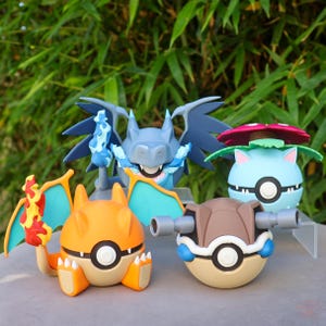 Könnte beinhalten: Eine Sammlung farbenfroher Pokémon-Charakterfiguren. Die Figuren umfassen ein orangefarbenes Charizard mit Flammen, einen blauen Drachen, eine braune Schildkröte und eine blau-rosa blütenartige Kreatur.