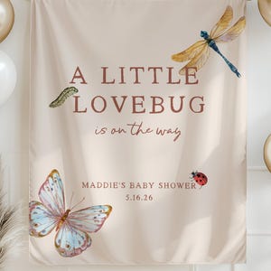 May include: A baby shower banner with the text "A Little Lovebug is on the way." The banner features illustrations of a butterfly, dragonfly, ladybug, and caterpillar. Gold and white balloons are on either side of the banner.