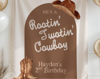 May include: A brown and white birthday banner with the text "He's a Rootin' Tootin' Cowboy" and "Hayden's 2nd Birthday". The banner features a cowboy hat and boots illustration. Gold and white balloons and a gold banner are also visible.