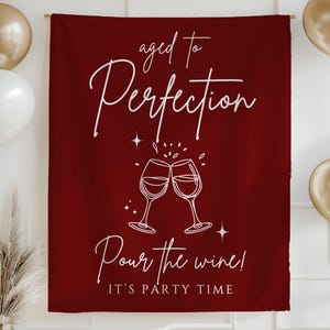 May include: A burgundy party banner with white script that reads "aged to Perfection" and "Pour the wine! It's party time". The banner features a graphic of two wine glasses clinking. Gold and white balloons and a gold banner are in the background.