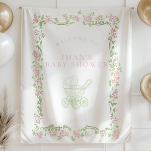 Pu&ograve; includere: Un banner di tessuto bianco con la scritta "Welcome to Iman's Baby Shower" in rosa e verde. Il banner &egrave; decorato con disegni floreali e un'illustrazione di un passeggino. Sono presenti anche palloncini dorati e bianchi e ghirlande triangolari dorate.