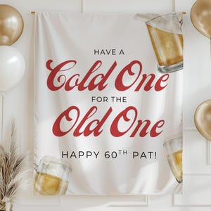 May include: White banner with red script reading "Have a Cold One for the Old One" and "Happy 60th Pat!". The banner features beer glasses and gold balloons. A gold vase with dried plants is in the corner, with gold bunting.