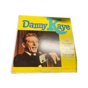 Może przedstawiać: Żółto-niebieska okładka albumu płytowego z fotografią Danny'ego Kaye'a i tekstem "Danny Kaye" w dużych, pogrubionych literach. Okładka albumu zawiera również tekst "z The Gingers Sisters, The Earl Brown Singers, Paul Weston and His Orchestra - prezentowane przez Twojego dealera Ramblera."