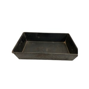 May include: A black metal baking pan with a rectangular shape. The pan has a slightly raised edge and a smooth surface.