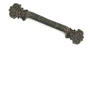 Könnte beinhalten: Ein dekorativer Türgriff aus Gusseisen mit einem verzierten Design. Der Griff ist dunkelbraun und hat einen langen, schlanken Griff.