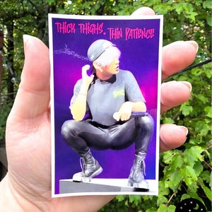 May include: A sticker with a purple background featuring an image of a person wearing a gray shirt, black pants, and boots. The sticker has the text "Thick Thighs. Thin Patience" in pink.