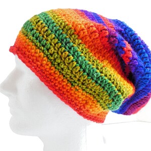 May include: A handmade, slouchy beanie hat in a vibrant rainbow of colors. The hat is crocheted with red, orange, yellow, green, blue, and purple yarn. The hat is shown on a white mannequin head.