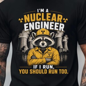 May include: Black t-shirt with a graphic of a raccoon wearing a yellow hard hat and jacket, with the text "I'M A NUCLEAR ENGINEER IF I RUN, YOU SHOULD RUN TOO." The raccoon is in front of a nuclear power plant.