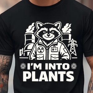 May include: Black t-shirt with a white graphic of a raccoon wearing a jacket, with the text "I'M INTO PLANTS". The design includes factory smokestacks, power lines, and atom symbols.
