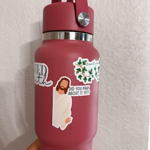 Op de afbeelding: Een bordeauxrode ge&iuml;soleerde waterfles met een handvat en zilveren accenten. De fles is versierd met stickers, waaronder een van Jezus en de zin "Did you pray about it yet?"