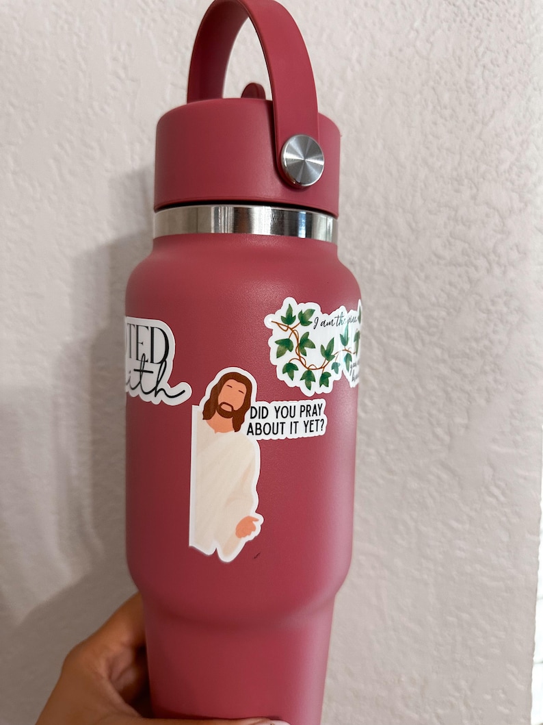 Op de afbeelding: Een bordeauxrode ge&iuml;soleerde waterfles met een handvat en zilveren accenten. De fles is versierd met stickers, waaronder een van Jezus en de zin "Did you pray about it yet?"
