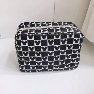 Op de afbeelding: Zwart-wit geruite make-uptas met Mickey Mouse-silhouetten. De tas heeft een rechthoekige vorm met een ritssluiting en een goudkleurige ritssluiting. De tas is gemaakt van een glanzend materiaal.