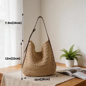 Op de afbeelding: Een beige geweven draagtas met bruine leren bandjes. De tas is 33 cm hoog, 38 cm breed en 20 cm diep. De tas staat op een houten tafel.