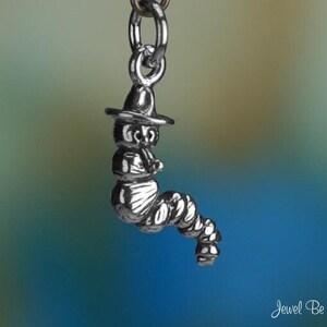 May include: Silver charm of a cartoon caterpillar wearing a hat. The charm is designed to be added to a bracelet or necklace.