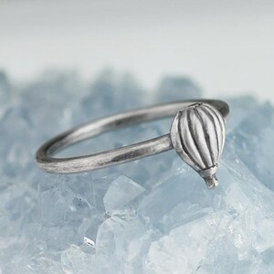 May include: A silver ring with a hot air balloon design. The balloon is detailed with vertical lines and a small basket at the bottom.