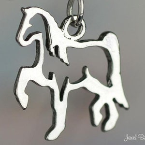 May include: A silver-colored pendant in the shape of a horse. The horse is stylized with a cutout design, showing the outline of the animal. The pendant is suspended from a small silver loop.
