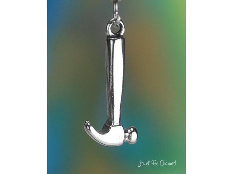 May include: A silver-colored hammer pendant with a rounded head and a long handle. The hammer is suspended from a small loop. The background is a gradient of blue, green, and yellow.