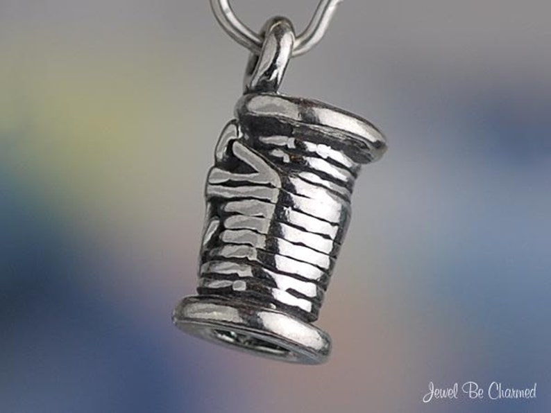 Puede incluir: Encanto de plata en forma de carrete de hilo. El encanto est&aacute; detallado con una superficie texturizada y un bucle para sujetarlo a una pulsera o collar.