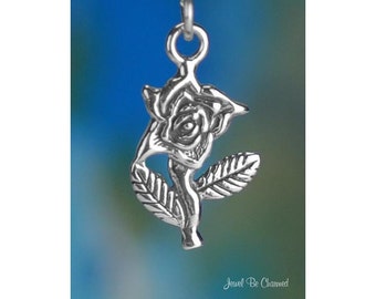 May include: A silver-colored pendant in the shape of a rose. The pendant features detailed leaves and petals, with a small loop at the top for a chain. The background is a blurred gradient of blue and green. The text "Jewel Be Charmed" is at the bottom.