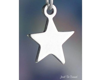 May include: A silver-colored star charm with a loop at the top for hanging. The star has five points and a smooth, reflective surface. The charm is suspended against a blurred blue and gray background.