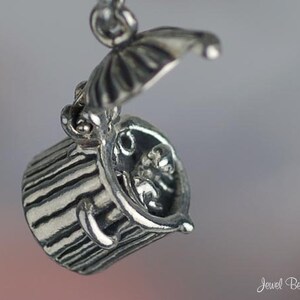 May include: A silver charm in the shape of a trash can with a lid that opens to reveal a small figure inside. The charm is detailed with textured lines and a hinged lid.