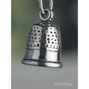 May include: A silver thimble charm with a textured surface. The charm is designed to look like a traditional thimble.