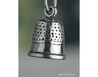 May include: A silver thimble charm with a textured surface. The charm is designed to look like a traditional thimble.