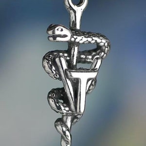 May include: A silver-toned pendant featuring the Rod of Asclepius, a symbol of medicine. The design includes a snake coiled around a staff, with the letters "VT" at the base. The pendant is suspended from a chain.