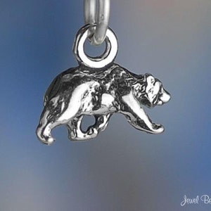 May include: A silver charm in the shape of a bear walking. The charm is detailed and has a smooth finish.