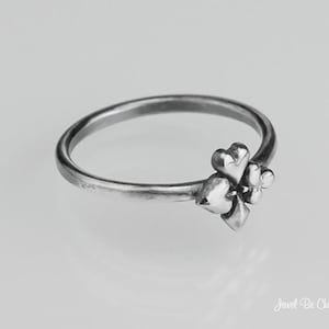 May include: A silver ring with a clover design. The clover is made up of four hearts.