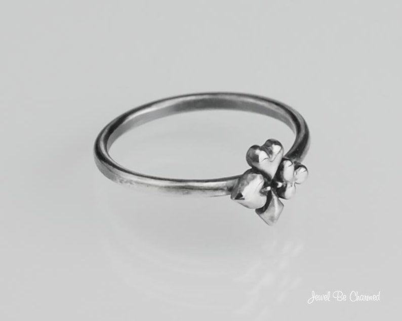 May include: A silver ring with a clover design. The clover is made up of four hearts.