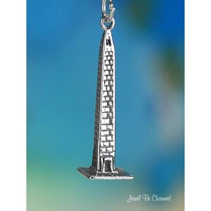 May include: A silver-colored charm in the shape of the Washington Monument. The charm is a detailed miniature replica of the obelisk, with a rectangular base and a pointed top. The charm is suspended from a small loop.