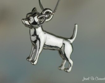 May include: A silver-toned metal charm shaped like a standing Chihuahua dog with pointed ears and an upright tail. The charm features a small circular loop at the top for attachment. The text Jewel Be Charmed is visible in the bottom right corner.