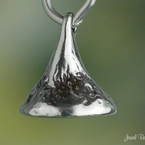 May include: A silver-colored pendant in the shape of a Hershey's Kiss, with a textured surface. The pendant is suspended from a silver loop. The background is a soft gradient of green and yellow.