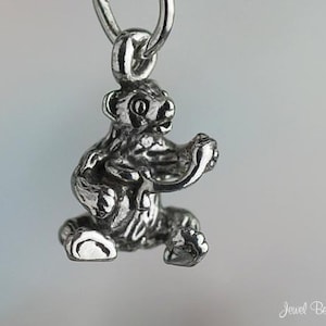 May include: A silver charm in the shape of a sitting bear. The bear is detailed with textured fur and has a playful expression.