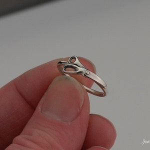 May include: A silver ring with a pair of scissors design. The ring is worn on a finger.