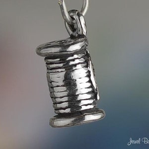 Puede incluir: Un charm de plata con forma de carrete de hilo. El charm est&aacute; detallado con una superficie texturizada y un bucle para sujetarlo a una pulsera o collar.