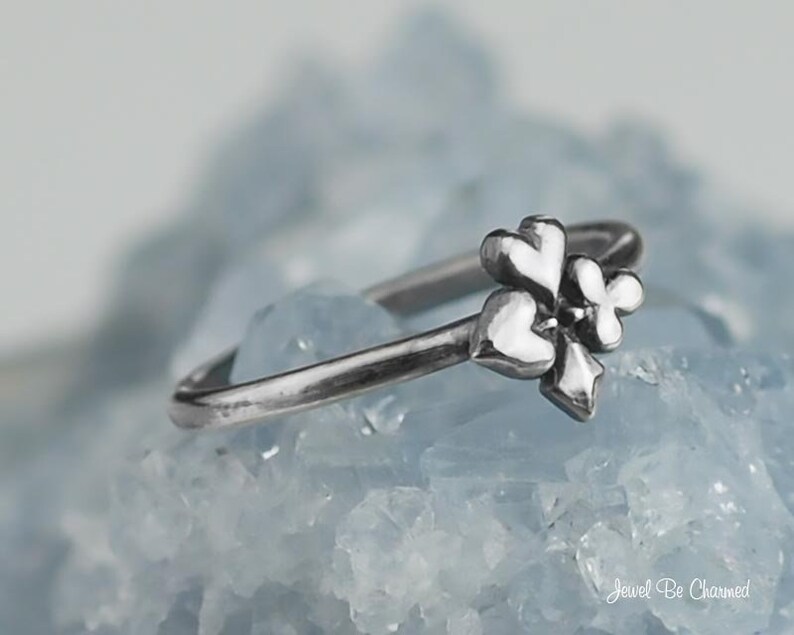 May include: A silver ring with a three-heart design. The ring is set on a bed of light blue crystals.