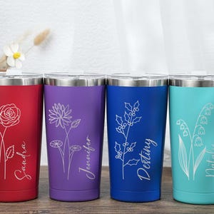 Puede incluir: Cuatro vasos de acero inoxidable en rojo, morado, azul y turquesa. Cada vaso presenta un diseño floral y un nombre en fuente cursiva. El vaso rojo tiene una rosa, el morado un loto, el azul acebo y el turquesa lirio de los valles.