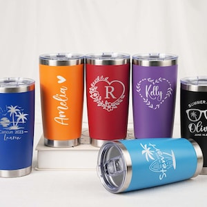 May include: A collection of personalized stainless steel tumblers in various colors, including blue, orange, red, purple, and black. Each tumbler features custom laser-engraved designs and text, such as names, dates, and graphics. The tumblers are designed for hot or cold beverages.