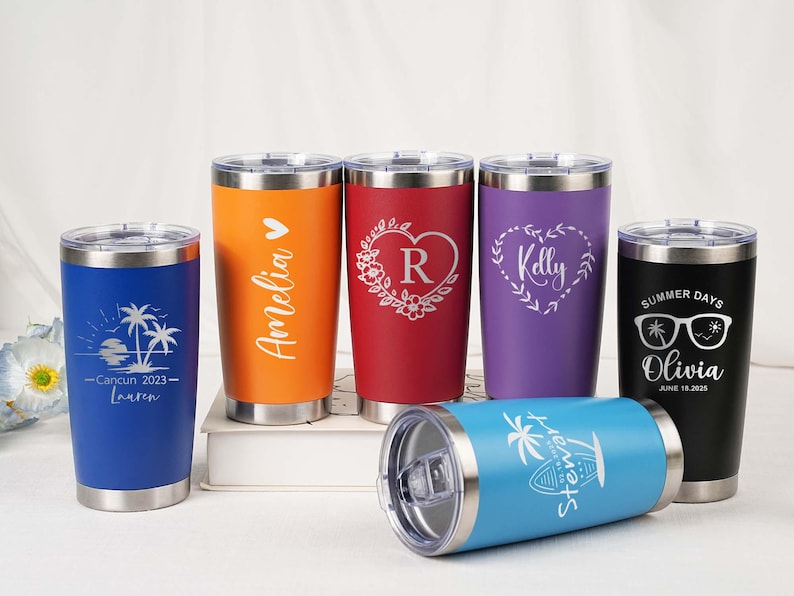 May include: A collection of personalized stainless steel tumblers in various colors, including blue, orange, red, purple, and black. Each tumbler features custom laser-engraved designs and text, such as names, dates, and graphics. The tumblers are designed for hot or cold beverages.